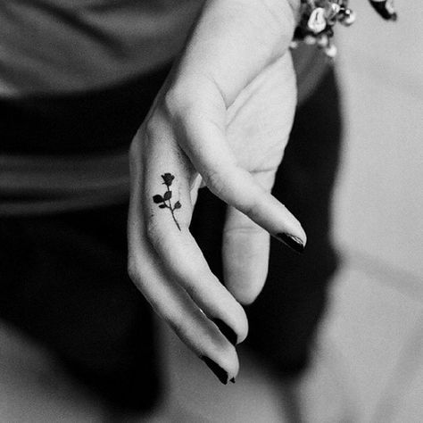 Incredibly tiny black rose tattoo on the middle finger