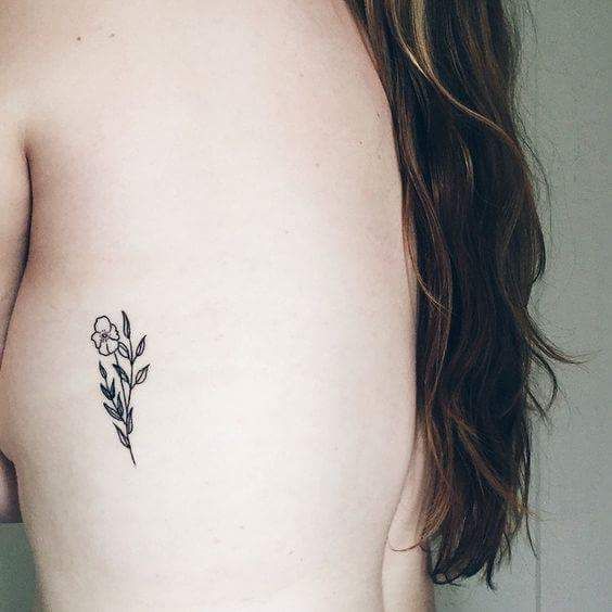 Delicate black tiny flower tattoo on the left rib