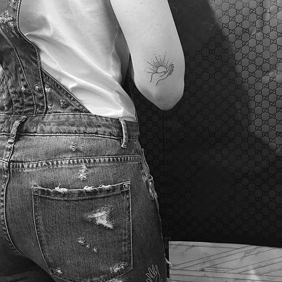 Hand holding a sun tattoo on the arm