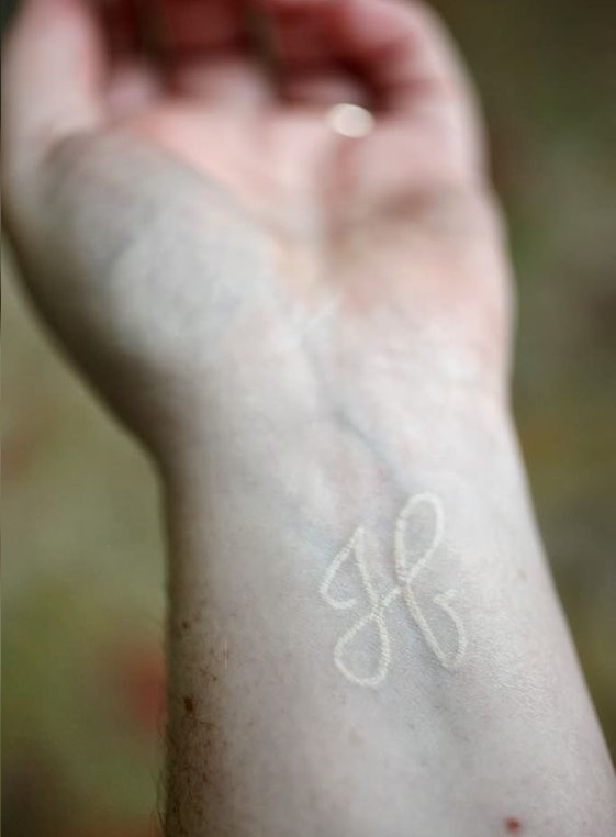 H initial tattoo in white on the wrist