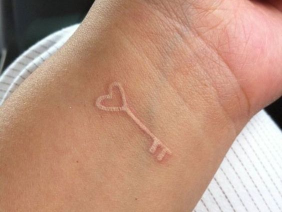 Small white key tattoo on the wrist
