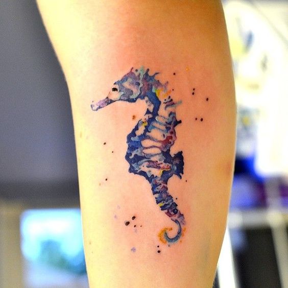 A watercolor tattoo of a seahorse on the arm