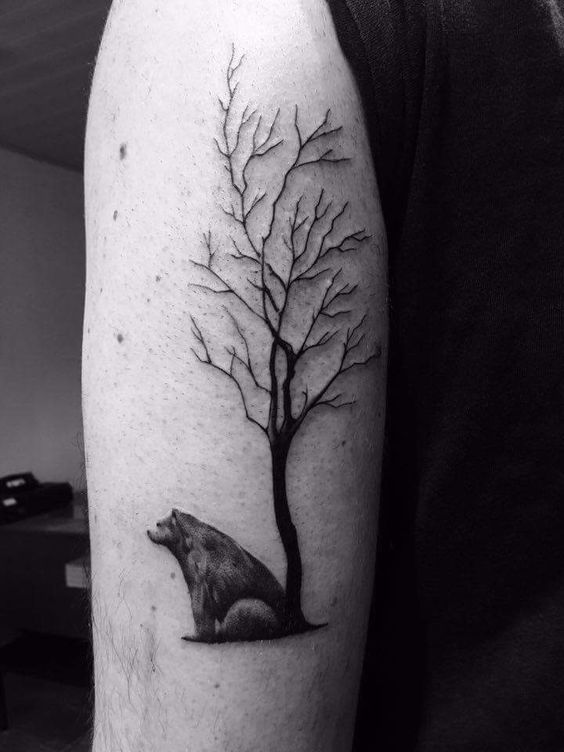 Bear sitting near the tree tattoo on the left arm