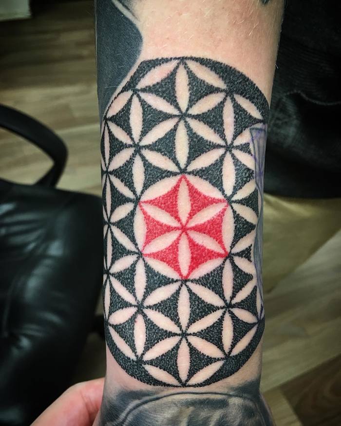 Black flower of life with a red center tattoo on the arm
