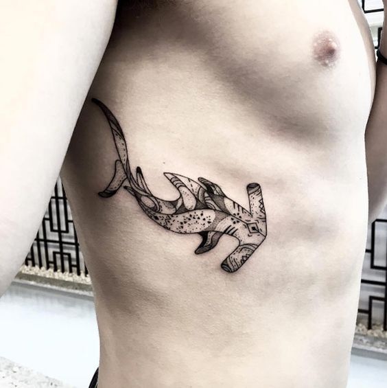 Black stylized tattoo of a hammerhead shark on the right rib cage