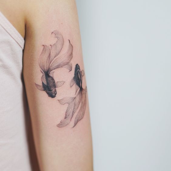 Black tattoo of two Koi Fish on the left arm