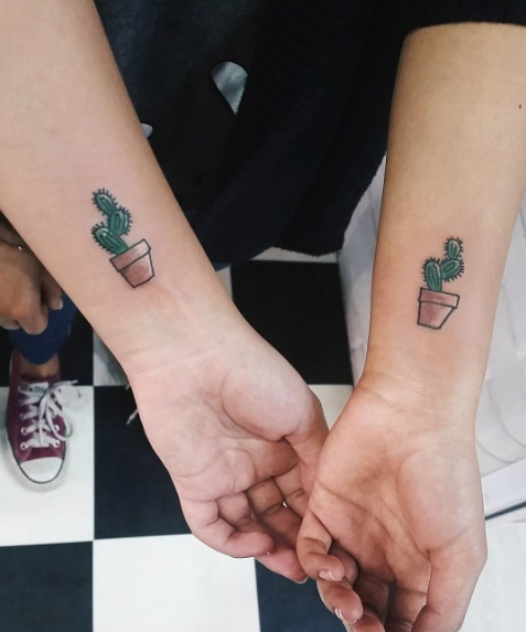 Matching small cactus in a pot tattoos on inner wrists