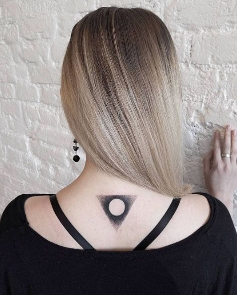 Negative space circle in a black triangle tattoo on the back