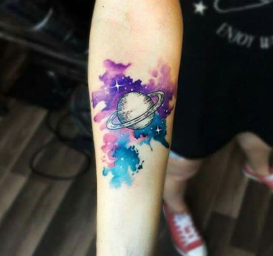 Saturn in watercolor cosmic background tattoo on the arm