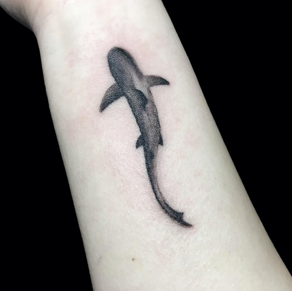 Small black tattoo of a shark on the inner wrist