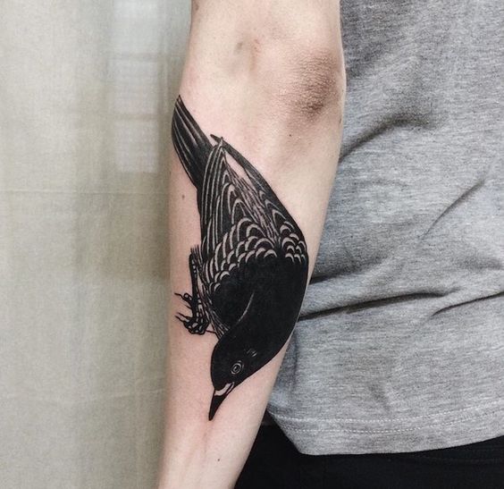 Solid black raven tattoo on the left forearm