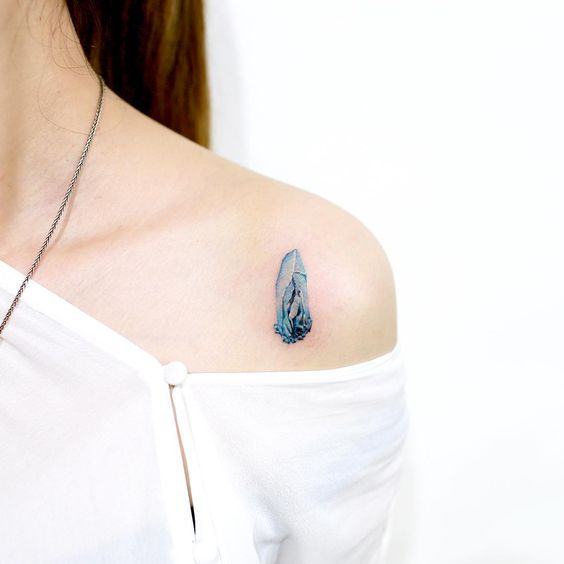 Tiny blue gemstone tattoo on the left shoulder