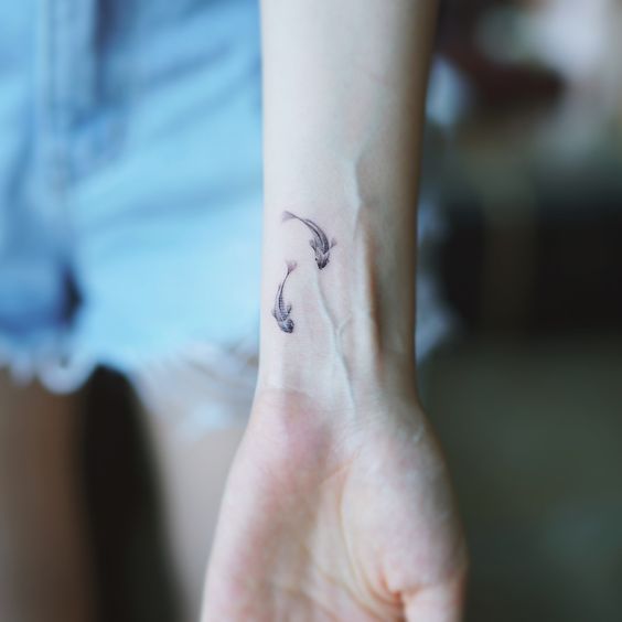 Tiny circular two fish tattoo on the wrist