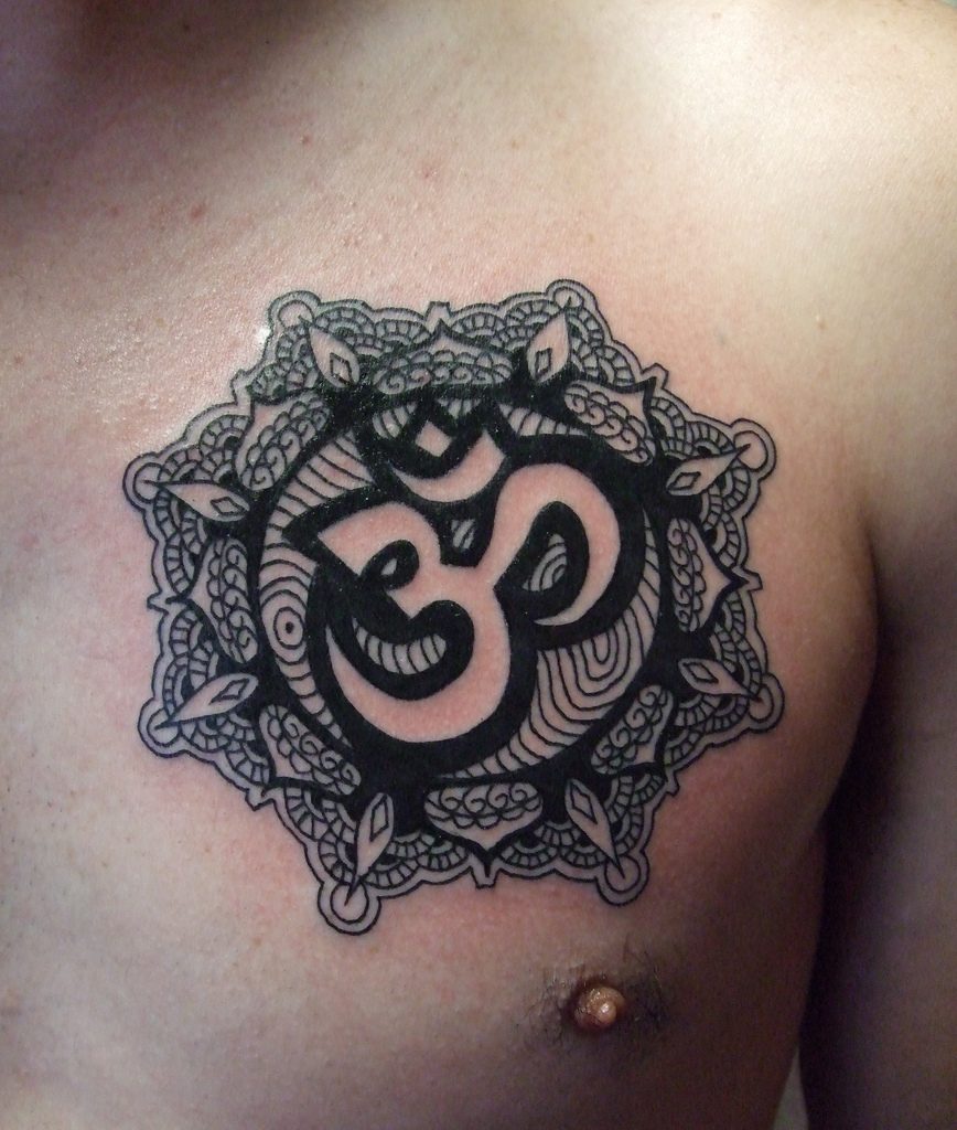 Black ornamental om tattoo on the chest