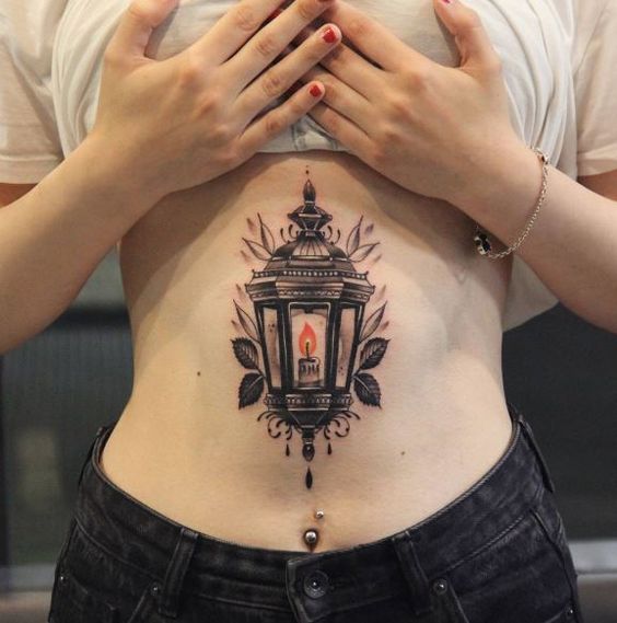 Burning candle inside a lantern tattoo on the belly