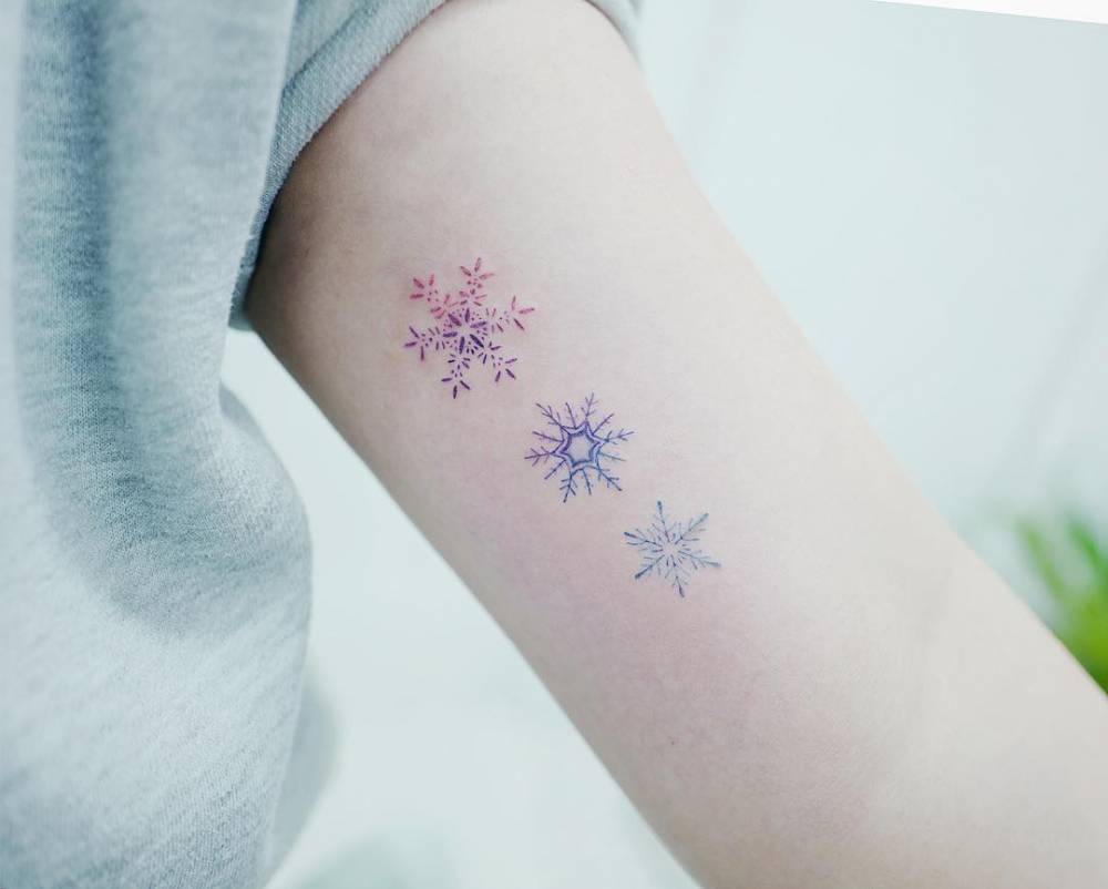 Gorgeous three blue and red snowflake tattoos on the upper left arm