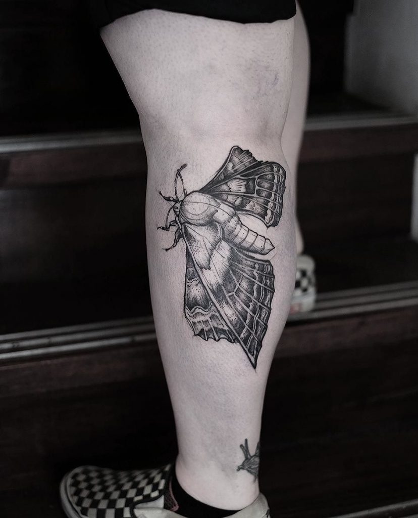 Hyper realistic black and grey moth on the left calf
