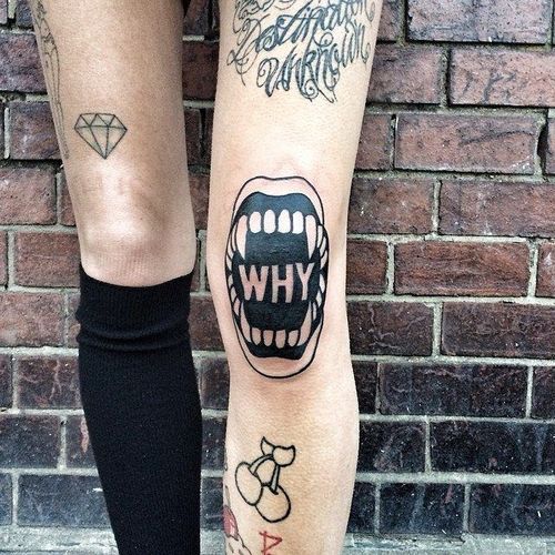 Negative space vampire jaw tattoo with the word why inked on the left knee