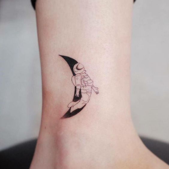 Small astronaut and crescent moon ankle tattoo