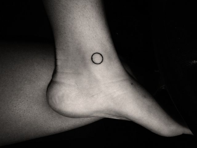 Black small circle tattoo on the ankle