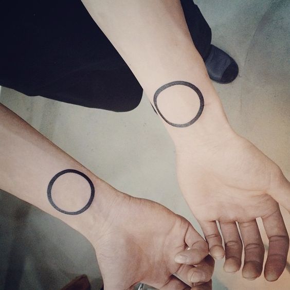 Matching black circle tattoos on the wrists