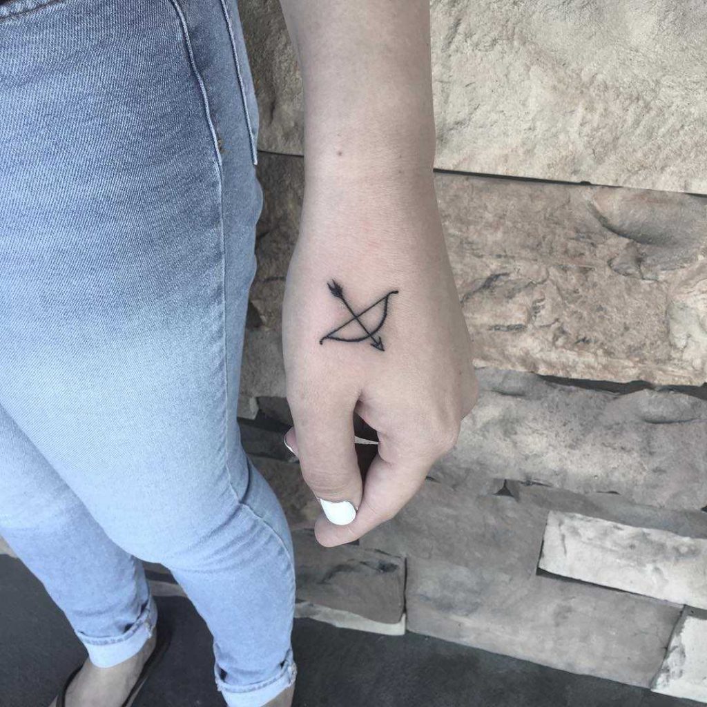 Small bow and arrow tattoo on the left hand by Andi Fitzpatrick